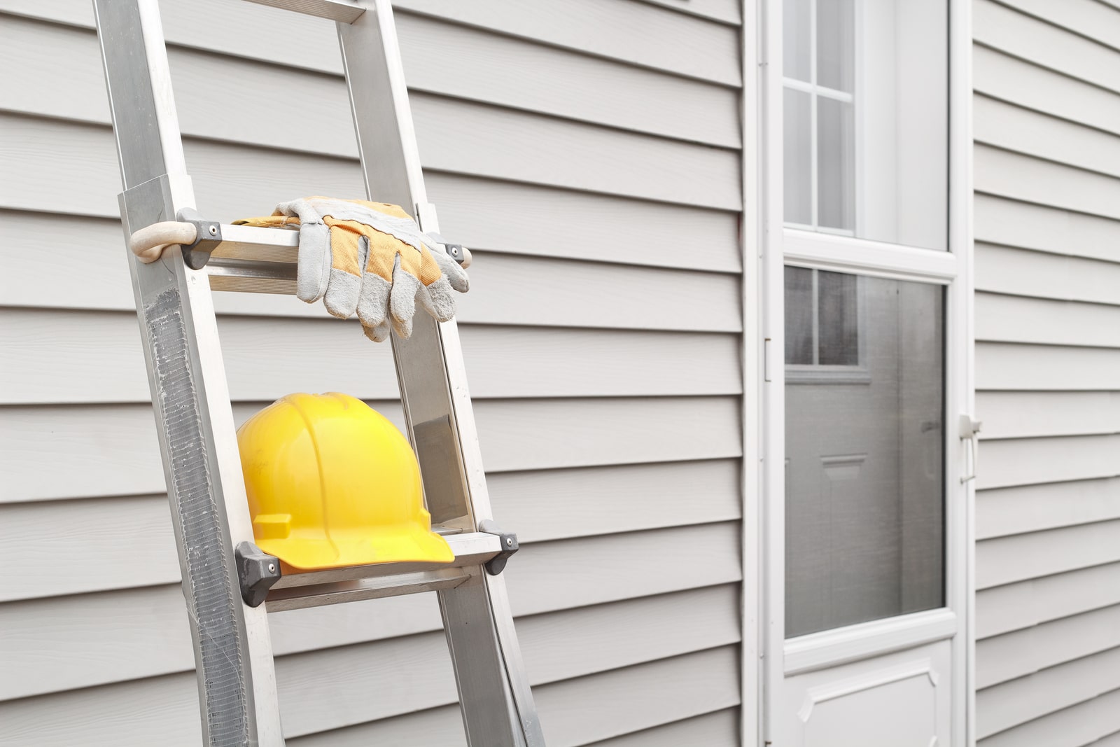 hard hat on ladder leaning against house, for roof repair job